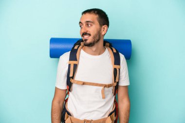 Mavi arka planda izole edilmiş beyaz yürüyüşçü gülümseyen, neşeli ve keyifli bir tarafa bakıyor..