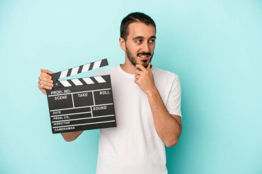 Beyaz tenli genç aktör elinde klaket tutuyordu. Mavi arka planda izole edilmişti. Bir şeyin fotokopi odasına baktığını sanıyordu..