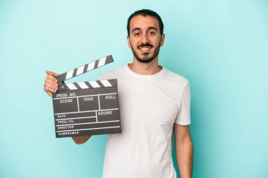 Kafkasyalı genç aktör elinde alkışlarla mavi arka planda izole edilmiş mutlu, güler yüzlü ve neşeli.