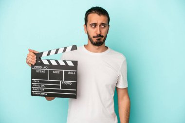 Kafkasyalı genç aktör elinde alçıpanla mavi arka planda izole edilmiş, kafası karışmış, şüpheli ve güvensiz hissediyor..