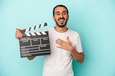 Beyaz tenli genç aktör, mavi arka planda izole edilmiş bir şekilde el ele tutuşarak gülüyor..