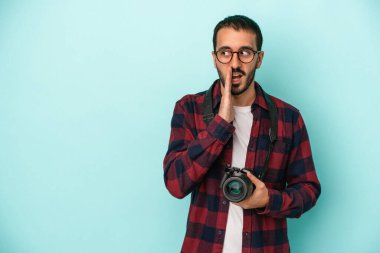 Kafkasyalı genç fotoğrafçı mavi arka planda izole edilmiş bir şekilde gizli bir sıcak fren haberi veriyor ve yana bakıyor.