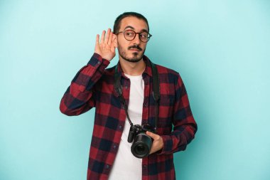Kafkasyalı genç fotoğrafçı mavi arka planda izole edilmiş bir şekilde bir dedikoduyu dinlemeye çalışıyor..