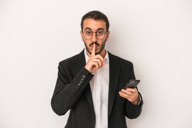 Beyaz arka planda izole edilmiş cep telefonu tutan genç bir iş adamı ya sır saklıyor ya da sessizlik istiyor..