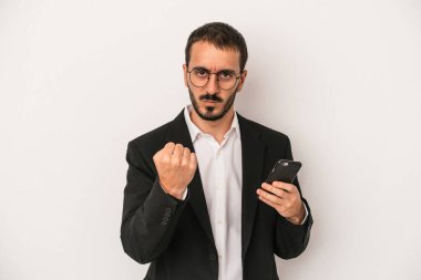 Beyaz arka planda izole edilmiş cep telefonu tutan genç bir iş adamı yumruğunu kameraya gösteriyor, agresif yüz ifadesi var..
