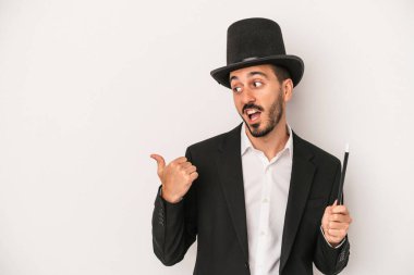 Genç sihirbaz sihirli değneğini beyaz arka plan noktalarında saklar başparmak uzakta, güler ve kaygısız.