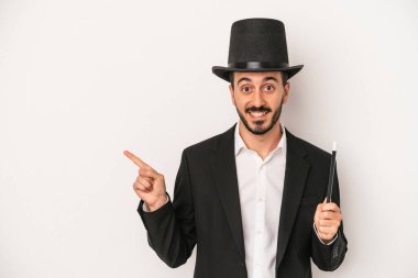 Beyaz arka planda bir değnek tutan genç sihirbaz gülümseyip işaret ediyor, boş alanda bir şey gösteriyor..