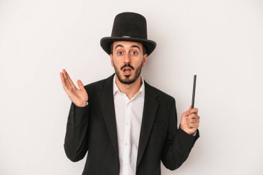 Genç sihirbaz sihirli değneği beyaz arka planda tutuyor. Şaşırmış ve şok olmuş..