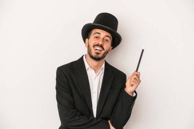 Genç sihirbaz sihirli değneği beyaz arka planda saklayıp gülüyor ve eğleniyor..