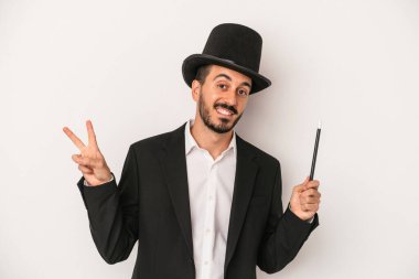 Genç sihirbaz sihirli değneği beyaz arka planda tutarak neşeli ve kaygısız bir barış sembolünü parmaklarıyla gösteriyor..