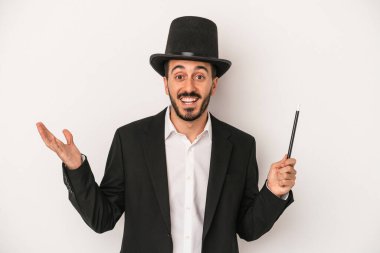 Beyaz arka planda asasını tutan genç sihirbaz hoş bir sürprizle karşılaşıyor, heyecanlı ve el kaldırıyor..