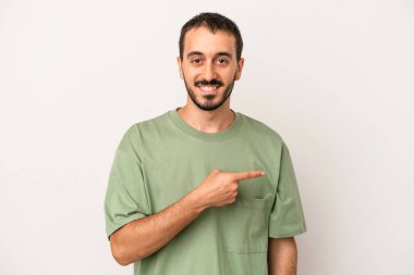 Beyaz arka planda izole edilmiş genç beyaz bir adam gülümsüyor ve boş alanda bir şeyler gösteriyor..