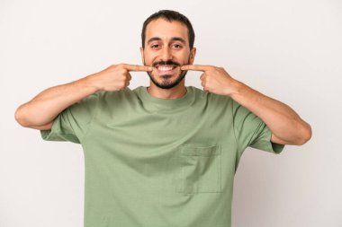 Beyaz arka planda izole edilmiş genç beyaz adam gülümsüyor, parmaklarını ağıza doğrultuyor..