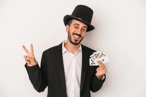 白い背景に孤立した魔法のカードを持っている若い魔術師の男喜びと屈託のない指で平和のシンボルを示す — ストック写真