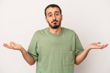 Beyaz arka planda izole edilmiş genç beyaz bir adam sorgulama sırasında omuz silkiyor ve şüphe duyuyor..