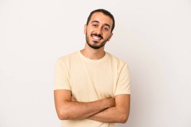 Beyaz arka planda kendini güvende hisseden, kararlılıkla kollarını kavuşturan beyaz tenli genç bir adam..