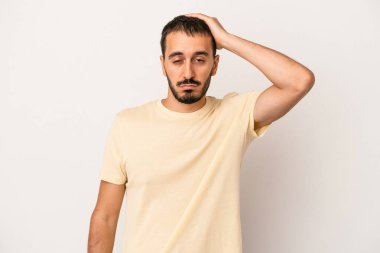 Beyaz arka planda izole edilmiş genç beyaz bir adam yorgun ve uykulu bir şekilde elini başının üstünde tutuyor..