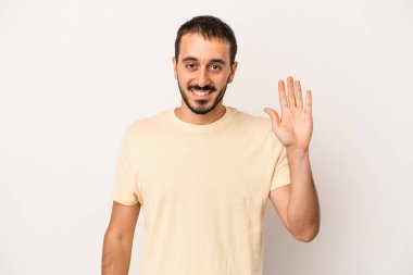 Beyaz arka planda izole edilmiş genç beyaz bir adam gülümseyerek beş numarayı parmaklarıyla gösteriyor..