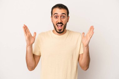 Beyaz arka planda izole olmuş genç beyaz bir adam zaferi veya başarıyı kutluyor, şaşırıyor ve şok oluyor..