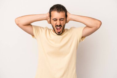 Beyaz arka planda izole edilmiş genç beyaz bir adam kulakları kulaklarıyla kapatıyor ve çok ses duymamaya çalışıyor..