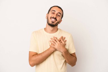 Beyaz arka planda soyutlanmış beyaz tenli genç bir adam gülüyor, elini yüreğine koyuyor, mutluluk kavramını koruyor..