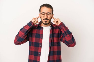 Beyaz arka planda izole edilmiş genç beyaz bir adam parmaklarıyla kulaklarını kapatıyor, gürültülü bir ortam yüzünden stresli ve çaresiz..