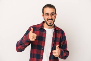 Beyaz arka planda izole edilmiş genç beyaz bir adam iki parmağını da kaldırıyor, gülümsüyor ve kendinden emin..