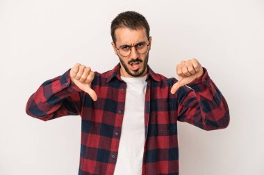 Beyaz arka planda izole edilmiş genç beyaz bir adam baş parmağını aşağı gösteriyor ve hoşlanmadığını ifade ediyor..