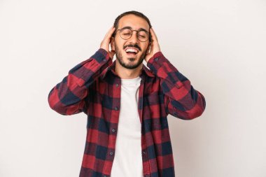 Beyaz arka planda izole olmuş genç beyaz bir adam ellerini başının üstünde tutarak neşeyle gülüyor. Mutluluk kavramı.