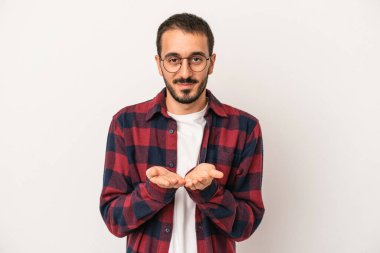 Beyaz arka planda izole edilmiş genç beyaz bir adam elinde avuç içi bir şeyle kameraya sunuyor..