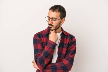Beyaz arka planda izole edilmiş genç beyaz bir adam şüpheli ve şüpheci bir ifadeyle yana bakıyor..