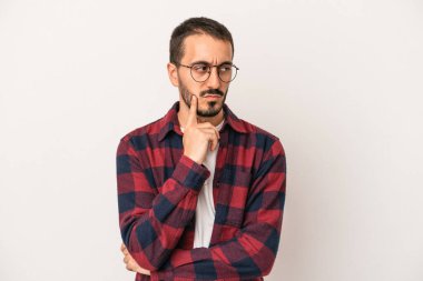 Beyaz arka planda izole edilmiş genç beyaz bir adam şüpheli ve şüpheci bir ifadeyle yana bakıyor..