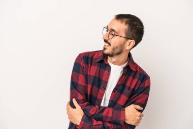 Beyaz arka planda izole edilmiş genç beyaz adam kollarını kavuşturarak gülümsüyor..