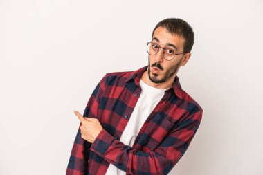 Beyaz arka planda izole edilmiş genç beyaz bir adam gülümsüyor ve boş alanda bir şeyler gösteriyor..