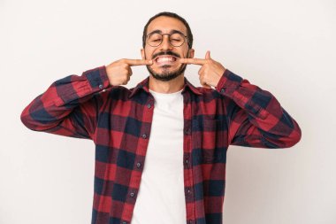 Beyaz arka planda izole edilmiş genç beyaz adam gülümsüyor, parmaklarını ağıza doğrultuyor..