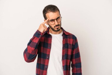 Beyaz arka planda izole edilmiş genç beyaz bir adam şakağı parmağıyla işaret ediyor, düşünüyor ve bir göreve odaklanıyor..