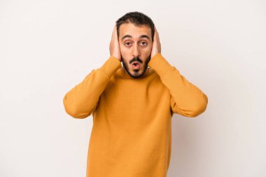 Beyaz arka planda izole edilmiş genç beyaz bir adam kulakları kulaklarıyla kapatıyor ve çok ses duymamaya çalışıyor..