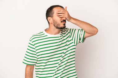 Beyaz arka planda soyutlanmış beyaz tenli genç bir adam elleriyle gözlerini kapatıyor, geniş bir gülümsemeyle bir sürpriz bekliyor..