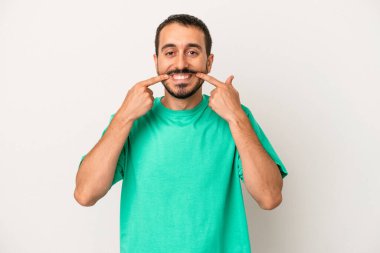 Beyaz arka planda izole edilmiş genç beyaz adam gülümsüyor, parmaklarını ağıza doğrultuyor..