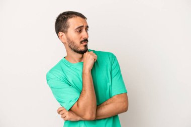 Beyaz arka planda soyutlanmış genç beyaz bir adam kafası karışmış, şüpheli ve güvensiz hissediyor..