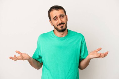 Beyaz arka planda izole edilmiş genç beyaz bir adam sorgulama sırasında omuz silkiyor ve şüphe duyuyor..