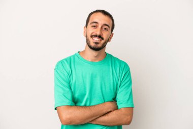 Beyaz arka planda kendini güvende hisseden, kararlılıkla kollarını kavuşturan beyaz tenli genç bir adam..