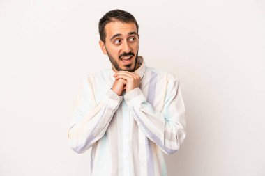 Beyaz arka planda izole edilmiş genç beyaz bir adam şans için dua ediyor, şaşırmış ve ağzını açıp önüne bakıyor..