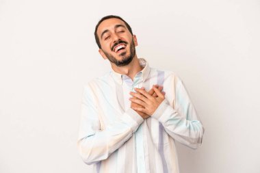 Beyaz arka planda soyutlanmış beyaz tenli genç bir adam gülüyor, elini yüreğine koyuyor, mutluluk kavramını koruyor..