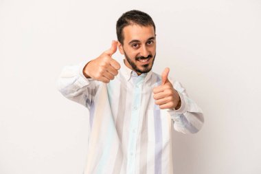 Beyaz arka planda izole edilmiş genç beyaz bir adam iki parmağını da kaldırıyor, gülümsüyor ve kendinden emin..