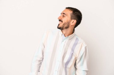Beyaz arka planda izole edilmiş genç beyaz adam gevşemiş ve mutlu bir şekilde gülüyor, boynunda dişlerini gösteriyor..