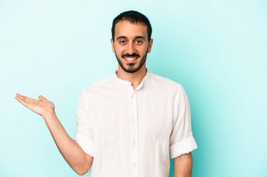 Mavi arka planda izole edilmiş genç beyaz bir adam bir palmiye üzerinde fotokopi alanı ve belinde bir el daha gösteriyor..