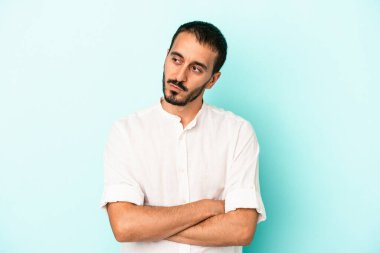 Mavi arka planda izole edilmiş genç beyaz adam kollarını kavuşturarak gülümsüyor..