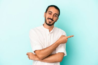 Mavi arka planda izole edilmiş genç beyaz adam işaret parmağıyla işaret ederek gülümsüyor..