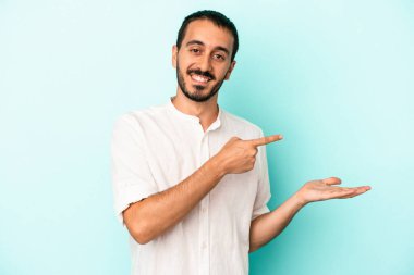 Kafkasyalı genç adam mavi arka planda izole edilmiş. Elinde palmiye ağacının bir kopyası olduğu için heyecanlı..